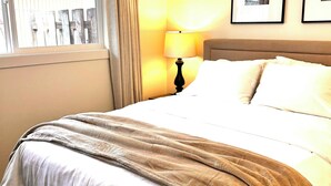 Et hotelværelse med seng, et vindue med gardiner, en lampe og to billeder i rammer på væggen.