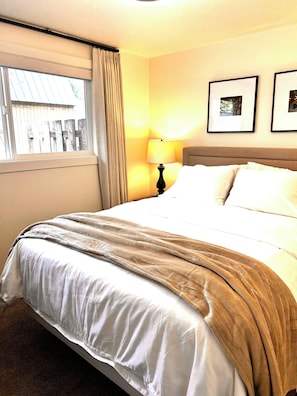 Habitación de hotel con cama, ventana con cortinas, lámpara y dos cuadros en la pared.