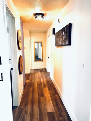 A hallway with wooden flooring, a door on the left, and a framed artwork on the right.