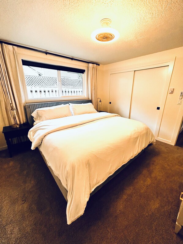 A hotel room with a bed, a window with curtains, a radiator, a door, and a light fixture on the ceiling.