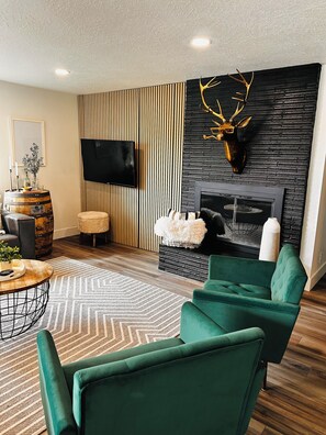 A modern living room with a fireplace, a mounted deer head, and a television on the wall.