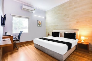 A hotel room with a bed, a desk, a chair, an air conditioner, a window, and a wall-mounted picture. - Collection O Bhiwadi (Bhiwadi)