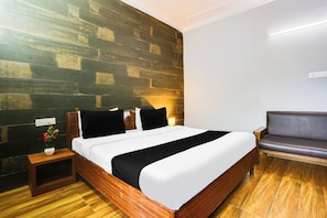 A hotel room with a wooden floor, a bed with white bedding, a nightstand with a vase of flowers, and a sofa. - Collection O Bhiwadi (Bhiwadi)