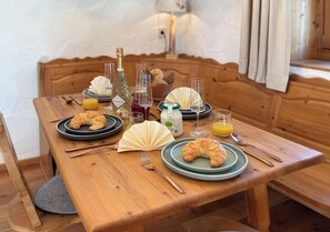 A wooden dining table set with plates, croissants, glasses, and a bottle of wine. - Holiday Apartment With 1 Bedroom (Garmisch-Partenkirchen)