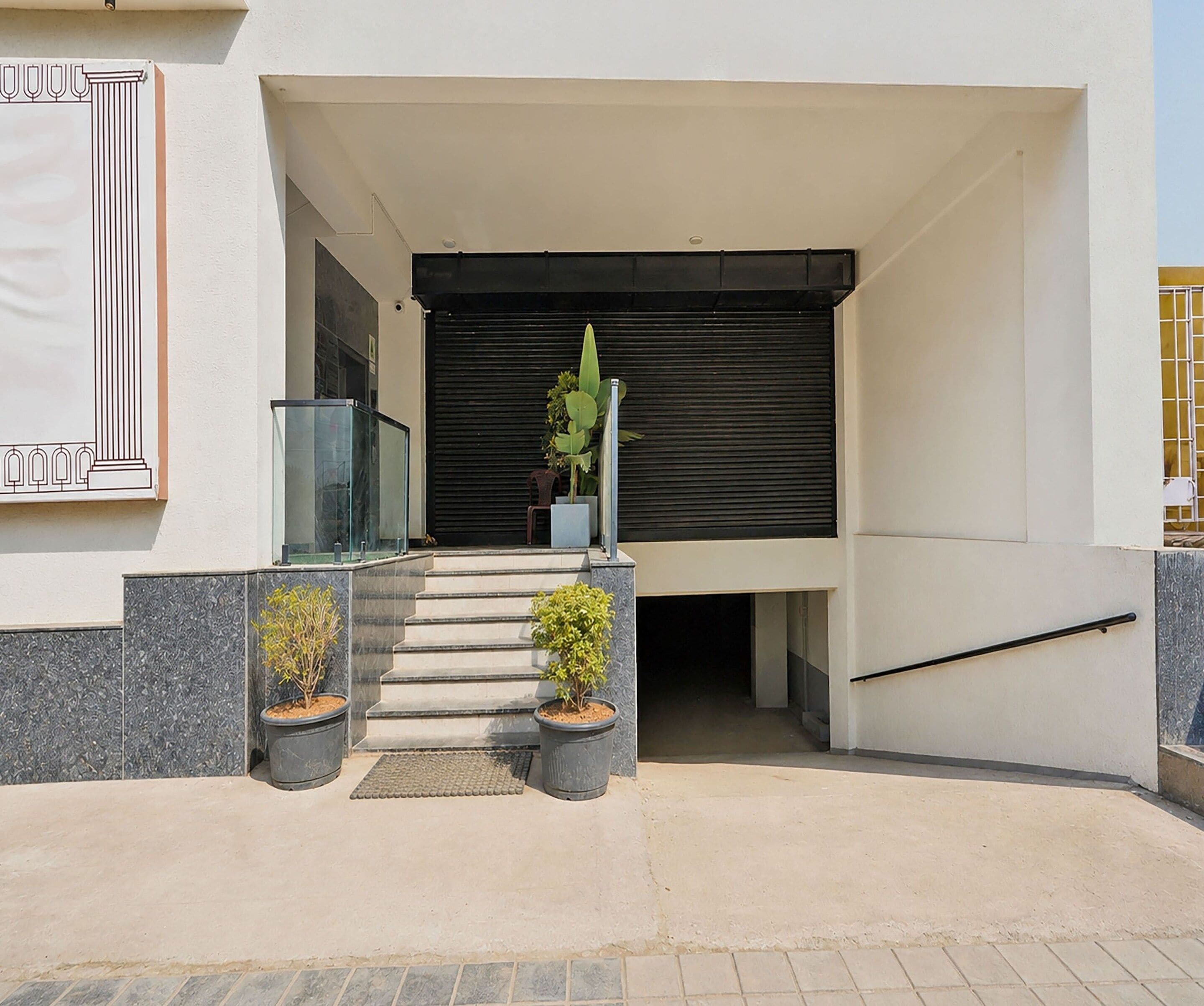 A modern entrance with a glass door, a set of stairs, and two potted plants.
