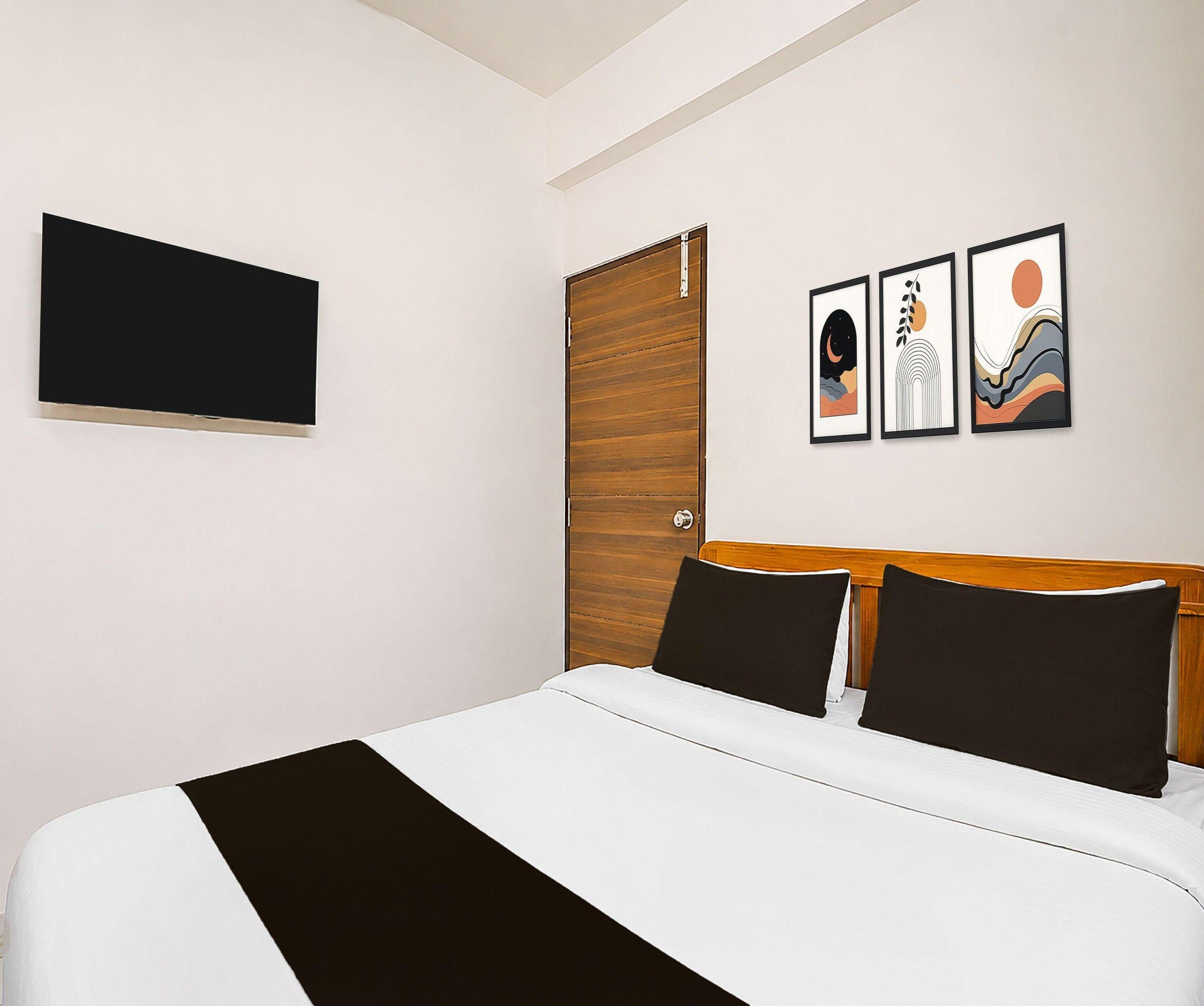 A hotel room with a bed, a TV mounted on the wall, and three framed artworks above the bed.