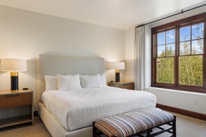 A hotel room with a large bed, two bedside lamps, a window with a view of trees, and a bench at the foot of the bed. - Outpost: Grand View 3220 - Has A/C! (Jackson)