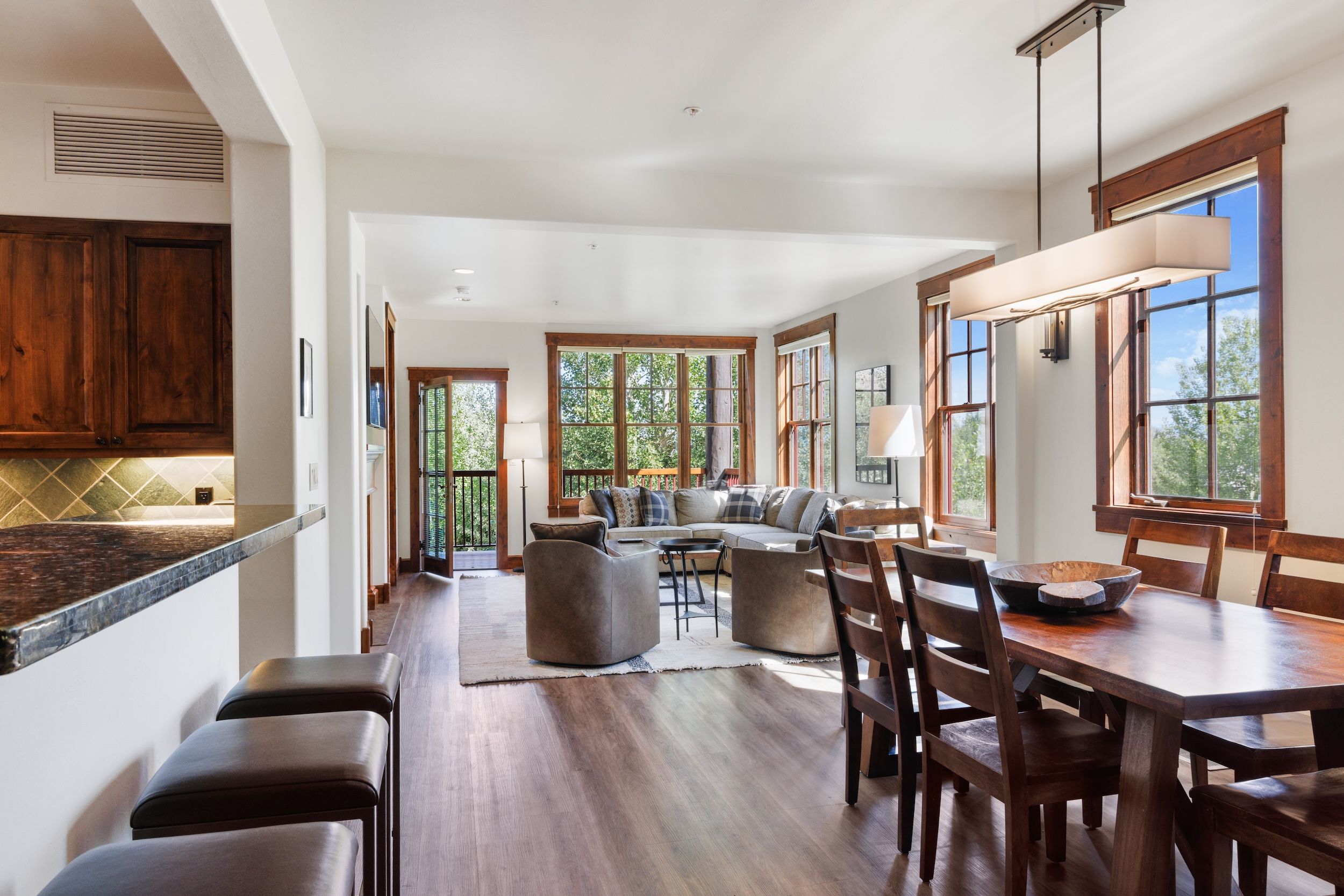 A spacious living area with a large window, a dining table, and a kitchen area with wooden cabinets.