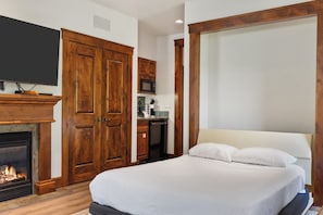 A bedroom with a bed, a television mounted on the wall, a fireplace, wooden wardrobes, and a kitchen area with a microwave. - Outpost: Grand View 322s - Has A/C (Jackson)
