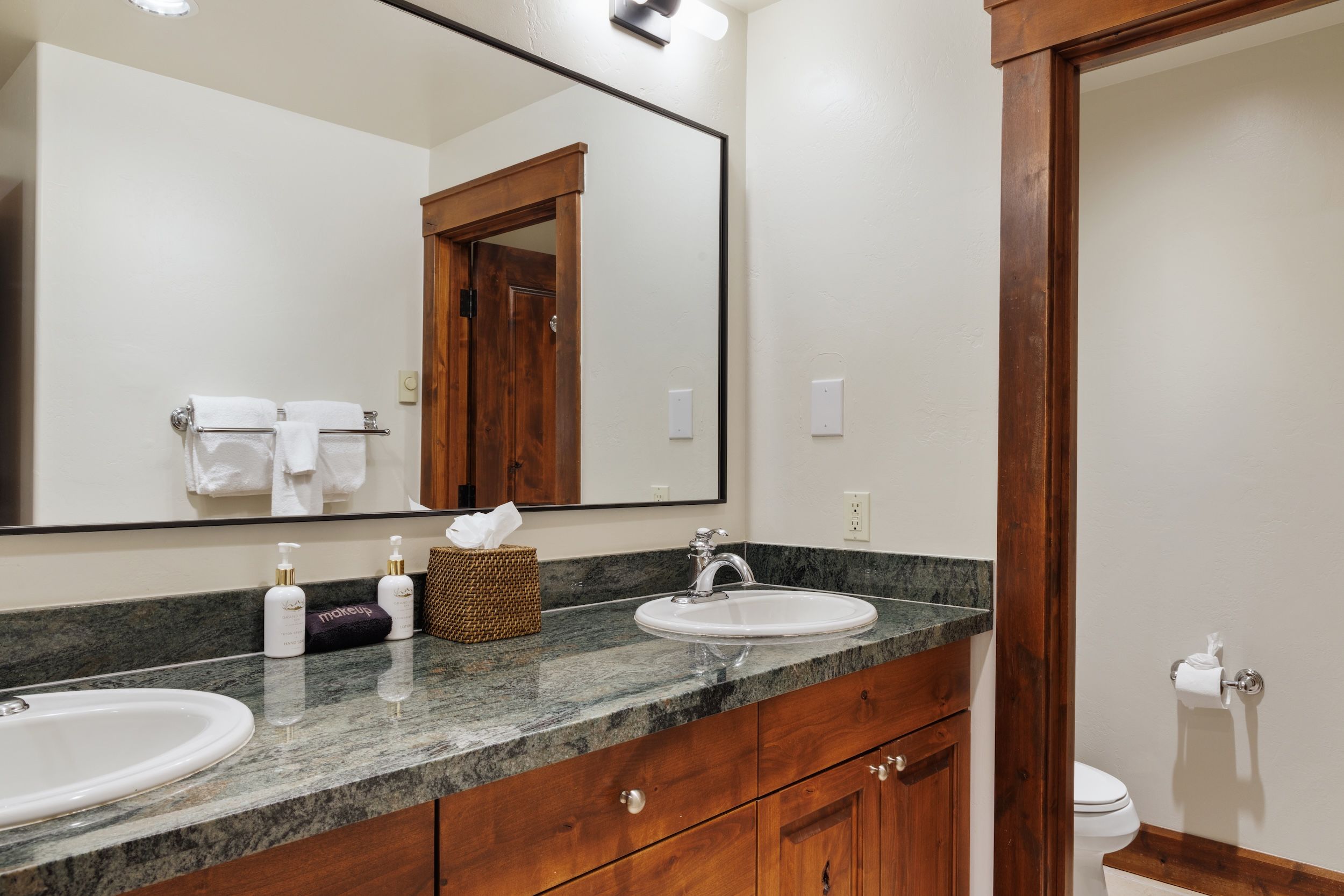 A bathroom with a large mirror, two sinks, a wooden vanity, and a toilet.