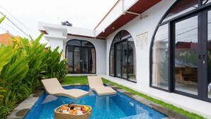 A modern outdoor pool area with two lounge chairs and a floating tray with food and drinks. - Aesthetic 3BR Bohemian Villa with Private Pool in Batu Bolong,Central Canggu (Badung)