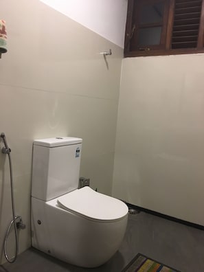 A bathroom with a toilet, a shower, and a window with blinds. - Cozy 2-bedroom house in tranquil Unawatuna with AC and fitness room (Unawatuna)