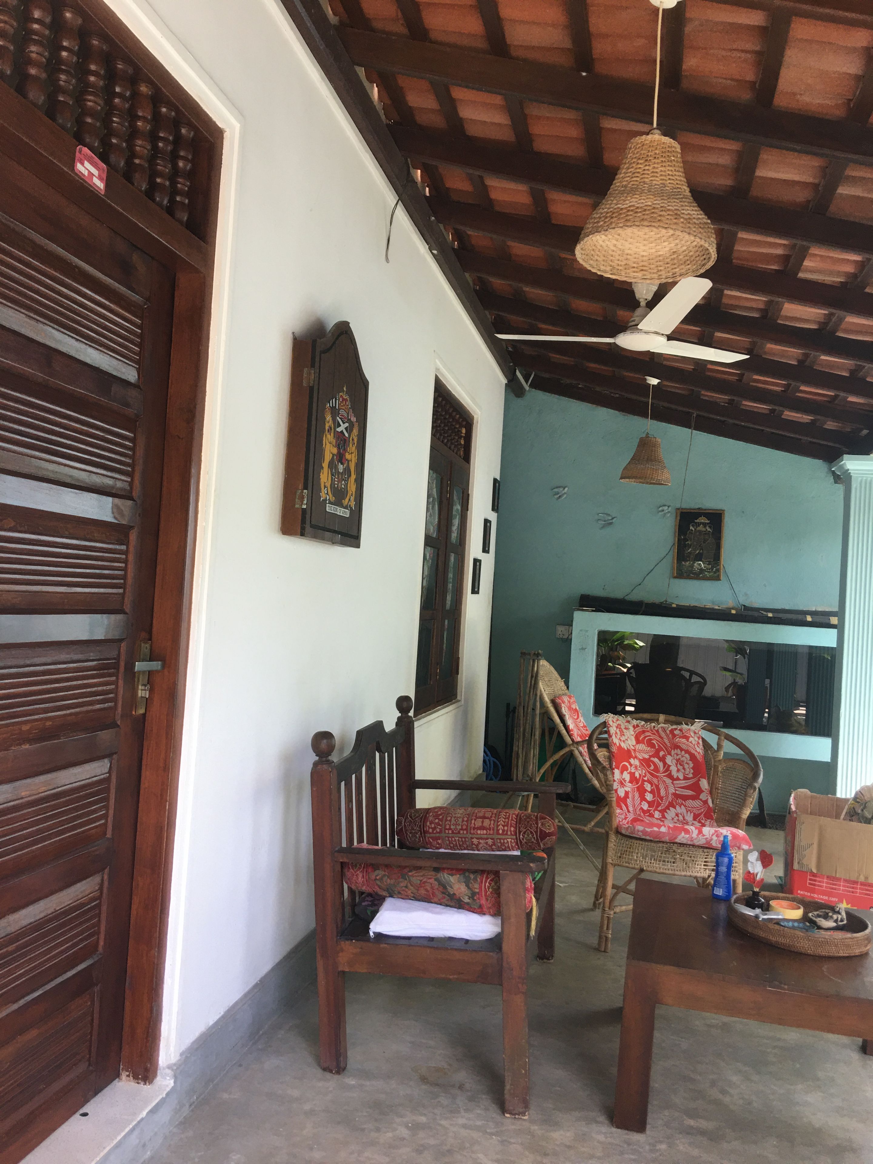 Quarto com porta de madeira, ventilador de teto, luminária de fibra natural e cadeira com almofada estampada.