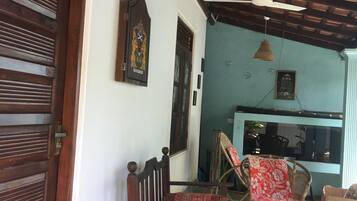 Quarto com porta de madeira, ventilador de teto, luminária de fibra natural e cadeira com almofada estampada.
