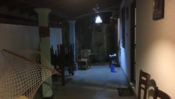 Un couloir faiblement éclairé, avec un hamac, des chaises et un ventilateur de plafond.
