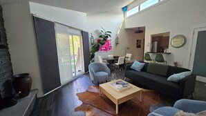 Ein modernes Wohnzimmer mit Kuhfellteppich, einer schwarzen Couch, einem Holztisch und einem Essbereich mit Tisch und Stühlen.