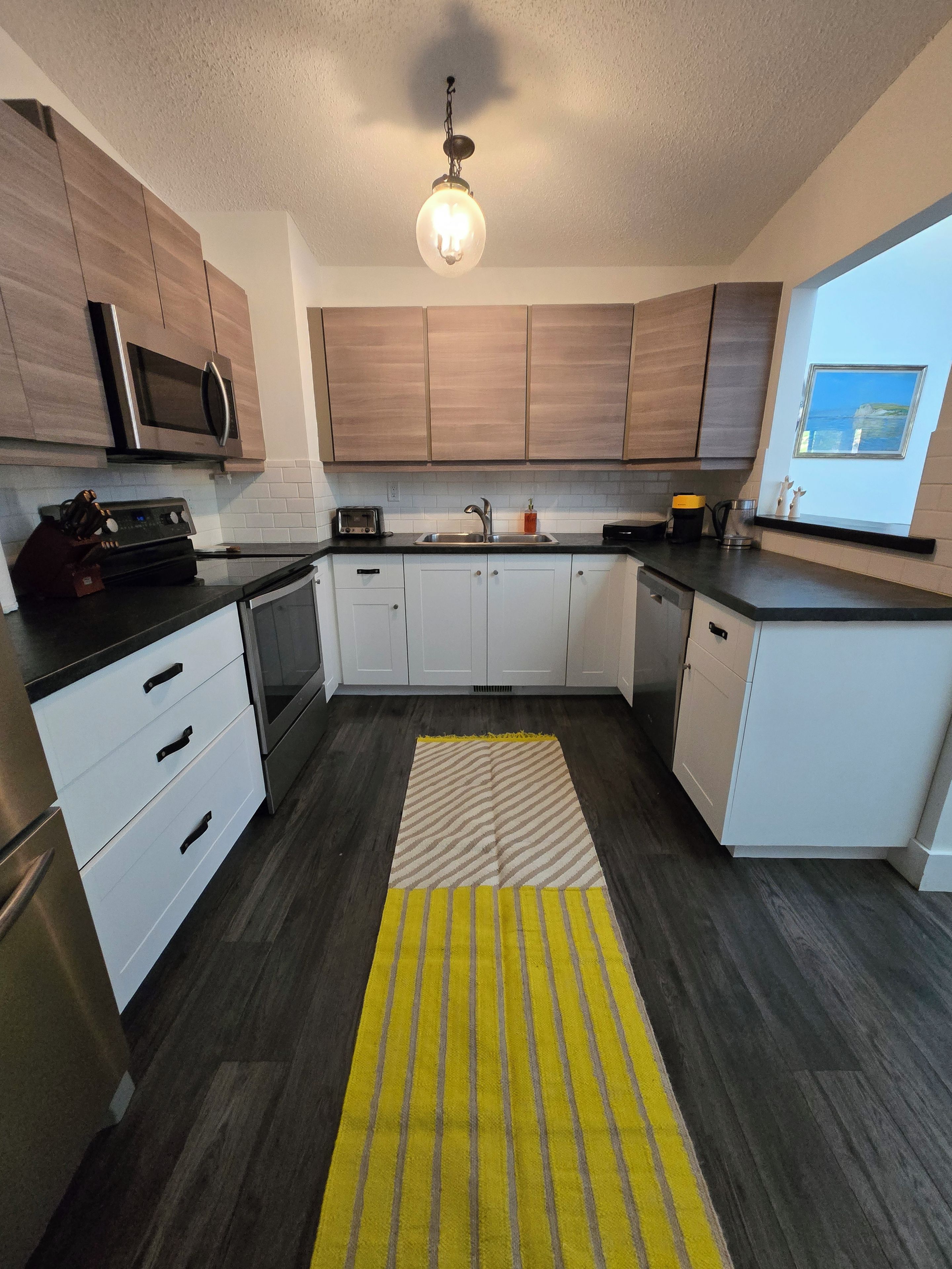 A modern kitchen with a microwave, toaster, sink, and a window with a view.