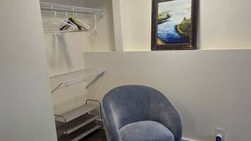 A room with a grey armchair, a painting on the wall, a white shelving unit, and a grey carpet.