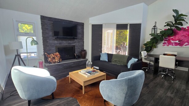 Ein modernes Wohnzimmer mit Kamin, Flachbildfernseher, einer Couch, zwei Sesseln, einem Couchtisch und einem Essbereich mit Tisch und Stühlen.