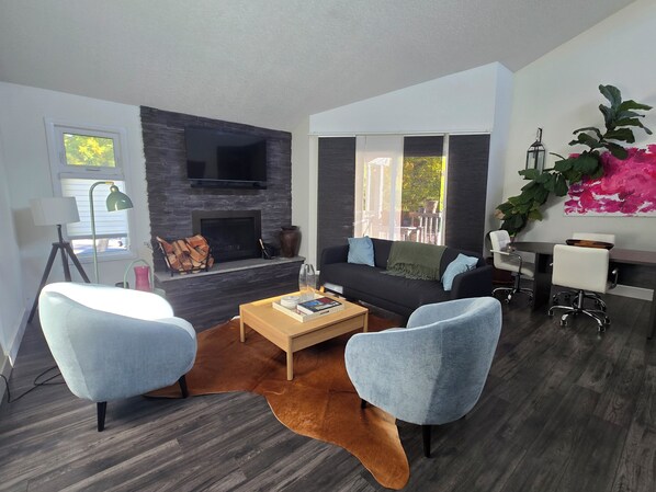 A modern living room with a fireplace, a flat-screen TV, a sofa, two armchairs, a coffee table, and a dining area with a table and chairs. - Luxury Family and Pet Friendly Apartment (Calgary)