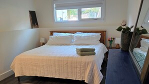 Ein Schlafzimmer mit einem Bett, einem runden Teppich, einer Kommode, einem Fenster und einer Pflanze.