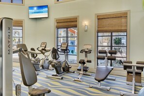 Une salle de sport équipée de divers appareils d’exercice, notamment des tapis de course et des appareils de musculation, et dotée de grandes fenêtres offrant une vue sur l’extérieur.