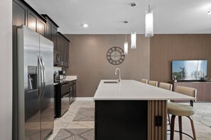 Une cuisine moderne dotée d’un grand îlot central, d’appareils électroménagers en acier inoxydable et d’une horloge murale.