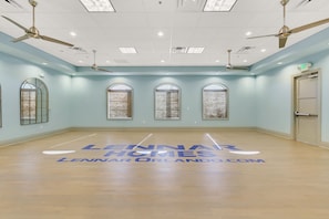 A spacious dance studio with a wooden floor, large windows with decorative curtains, ceiling fans, and a door with an exit sign. - 4BD/3BA Family Escape | Private Pool near Disney (Davenport)