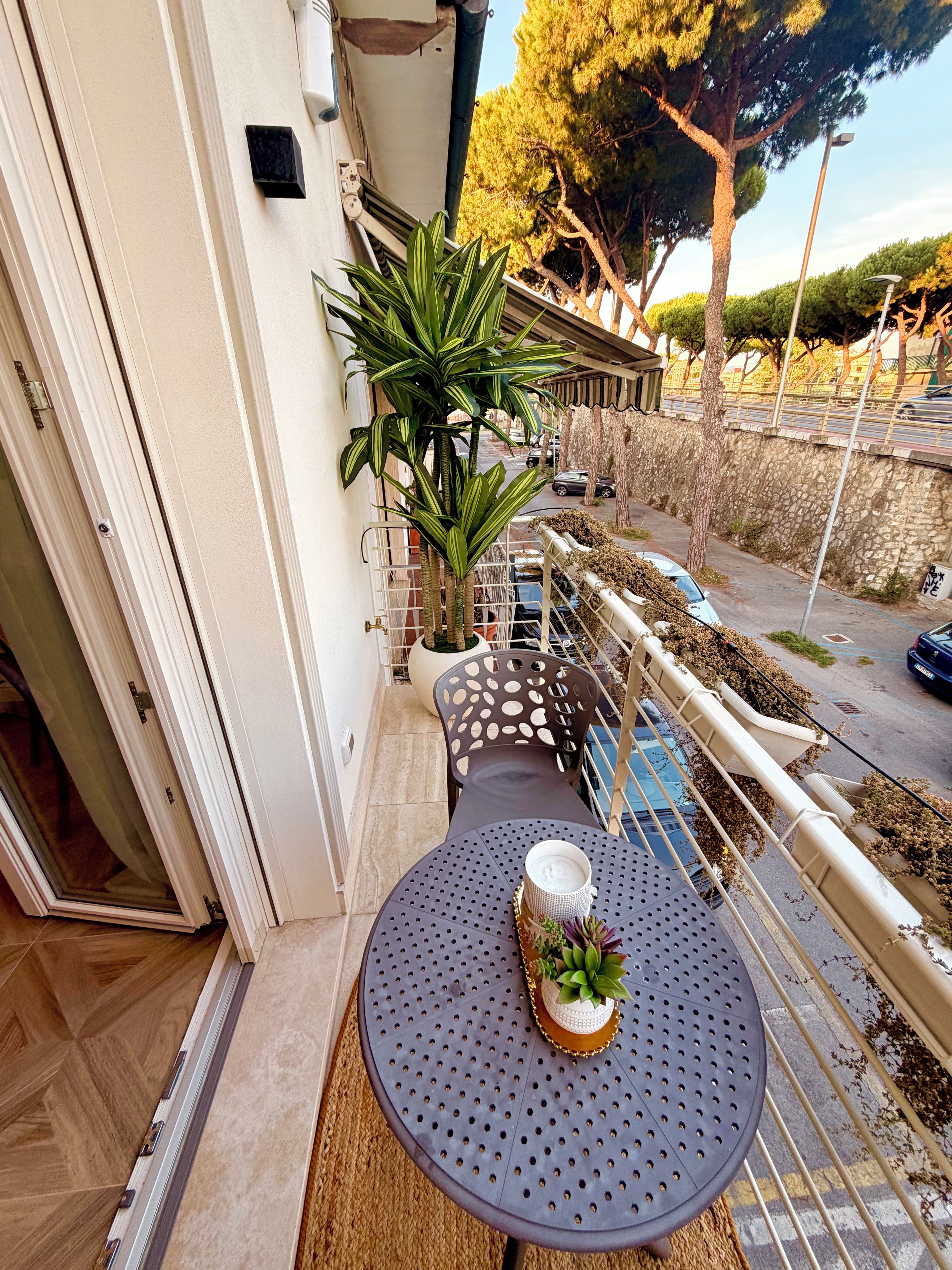Ein Balkon mit rundem Tisch, einer Topfpflanze und Blick auf die Straße.