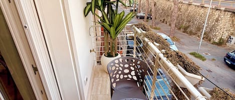 Een balkon met een ronde tafel, een plant in pot en uitzicht op de straat.