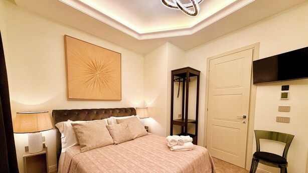 Une chambre d’hôtel avec un lit, une table de chevet, une lampe, un téléviseur fixé au mur et une porte.