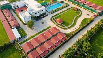 An aerial view of a hotel with a swimming pool, multiple buildings, and a well-maintained lawn.