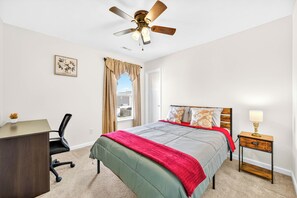 Ein Schlafzimmer mit Bett, Schreibtisch, Stuhl, Nachttisch, Lampe und Deckenventilator.