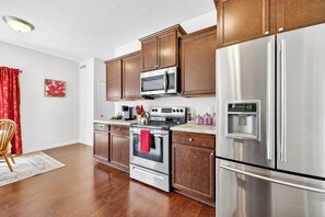 A modern kitchen with stainless steel appliances, wooden cabinets, and a red kettle on the stove.