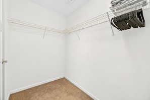 Ein Zimmer mit einer weißen Tür, einem Kleiderschrank mit Kleidung und einem Teppichboden.