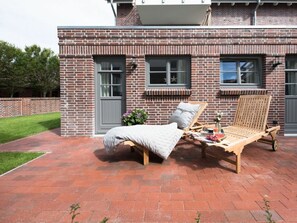 Ein Ziegelgebäude mit einer Terrasse, ausgestattet mit einem Bett, einer Liege und einem Tisch mit einem Getränk.