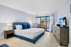 Habitación de hotel con una cama grande, un aparador de madera, un televisor y vista a la playa.