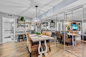 Una cocina moderna con salpicadero de piedra, un comedor con sillas de mimbre y un espejo grande que refleja el ambiente.