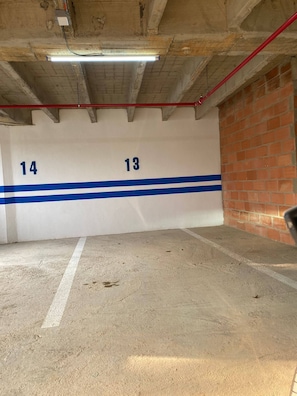 An indoor parking area with concrete floors and walls, marked parking spaces 13 and 14, and a red pipe on the ceiling. - Aves María 6th Floor With Balcony and Parking (Sabaneta)