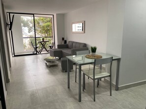 Ein modernes Wohnzimmer mit einem Glastisch, einem grauen Sofa und einer großen Schiebeglasdoor zum Balkon.