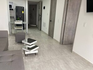 Ein modernes Wohnzimmer mit einem grauen Sofa, einem Glastisch und einem Essbereich mit weißem Tisch und Stühlen.