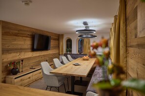 A modern dining area with a wooden table, grey upholstered chairs, and a flat-screen TV mounted on the wall. - Suite With Private Sauna (Gaschurn)
