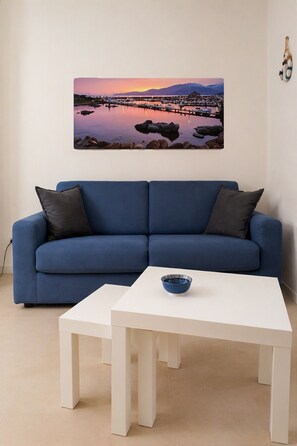 Ein modernes Wohnzimmer mit einem blauen Sofa, einem weißen Couchtisch und einem gerahmten Foto von einer Küstenlandschaft.