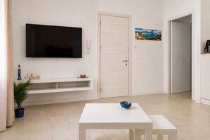 Een moderne woonkamer met een flatscreen televisie, een witte deur, een schilderij en een tafeltje met een schaal.