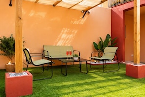 Un área de estar al aire libre con dos sillas y una mesa, rodeada de césped artificial y plantas en macetas.
