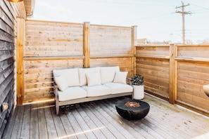 Una terraza de madera con un sofá blanco y una mesa redonda con un brasero.