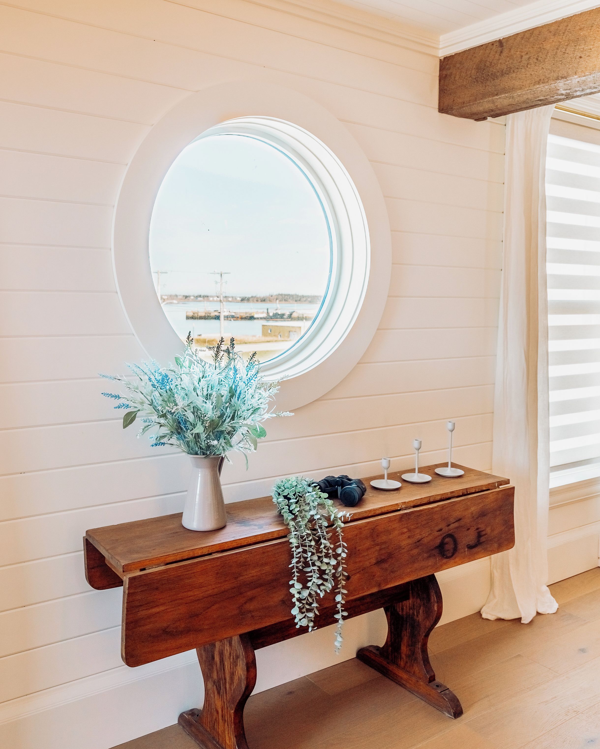 A wooden console table with a mirror, a vase with greenery, and a hanging plant.