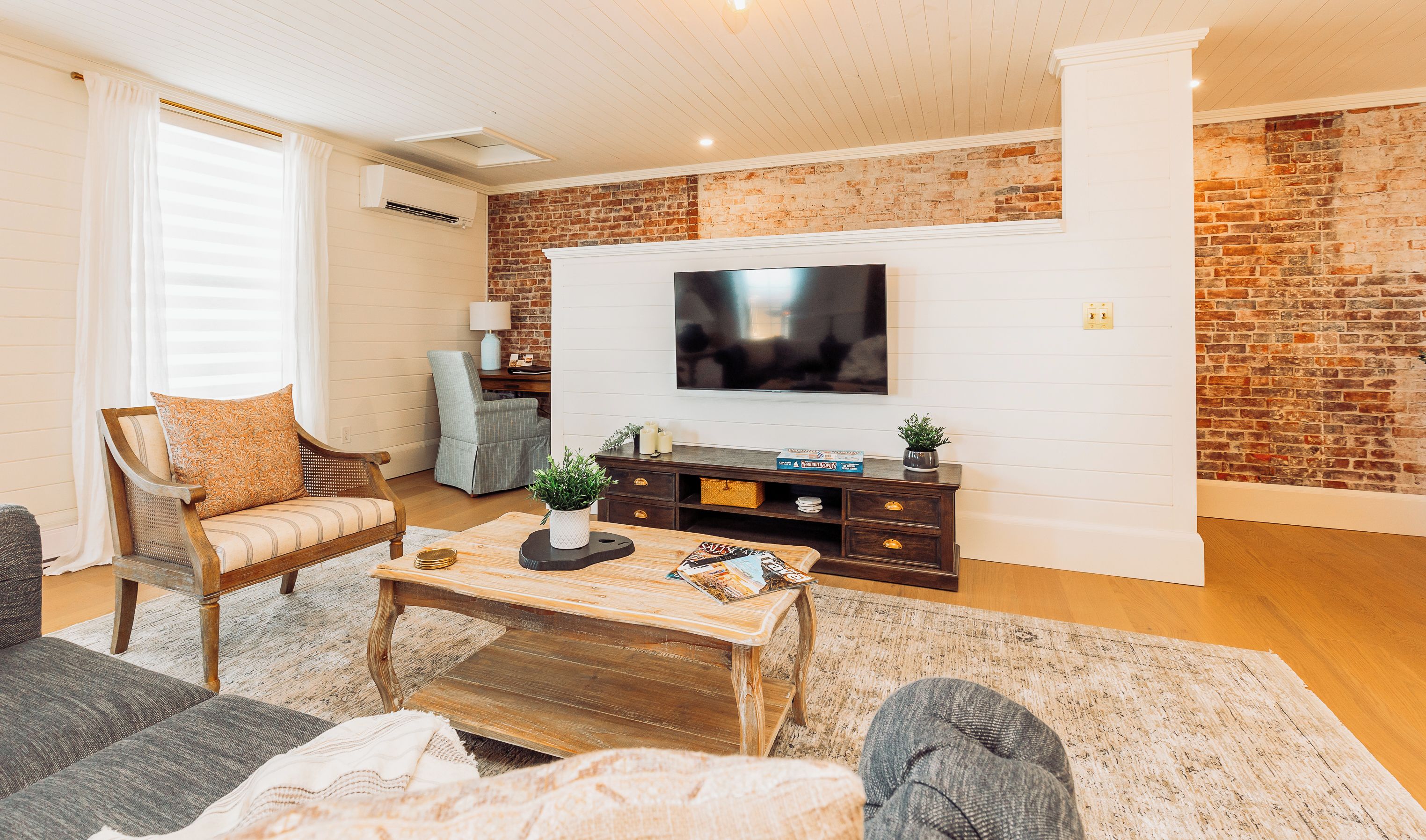 A living room with a brick wall, a flat-screen TV, a wooden coffee table, and a sofa.