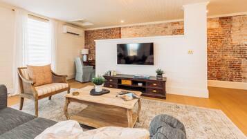 A living room with a brick wall, a flat-screen TV, a wooden coffee table, and a sofa.