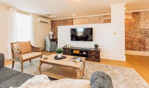 Un salon avec un mur en briques, un téléviseur à écran plat, une table basse en bois et un canapé.